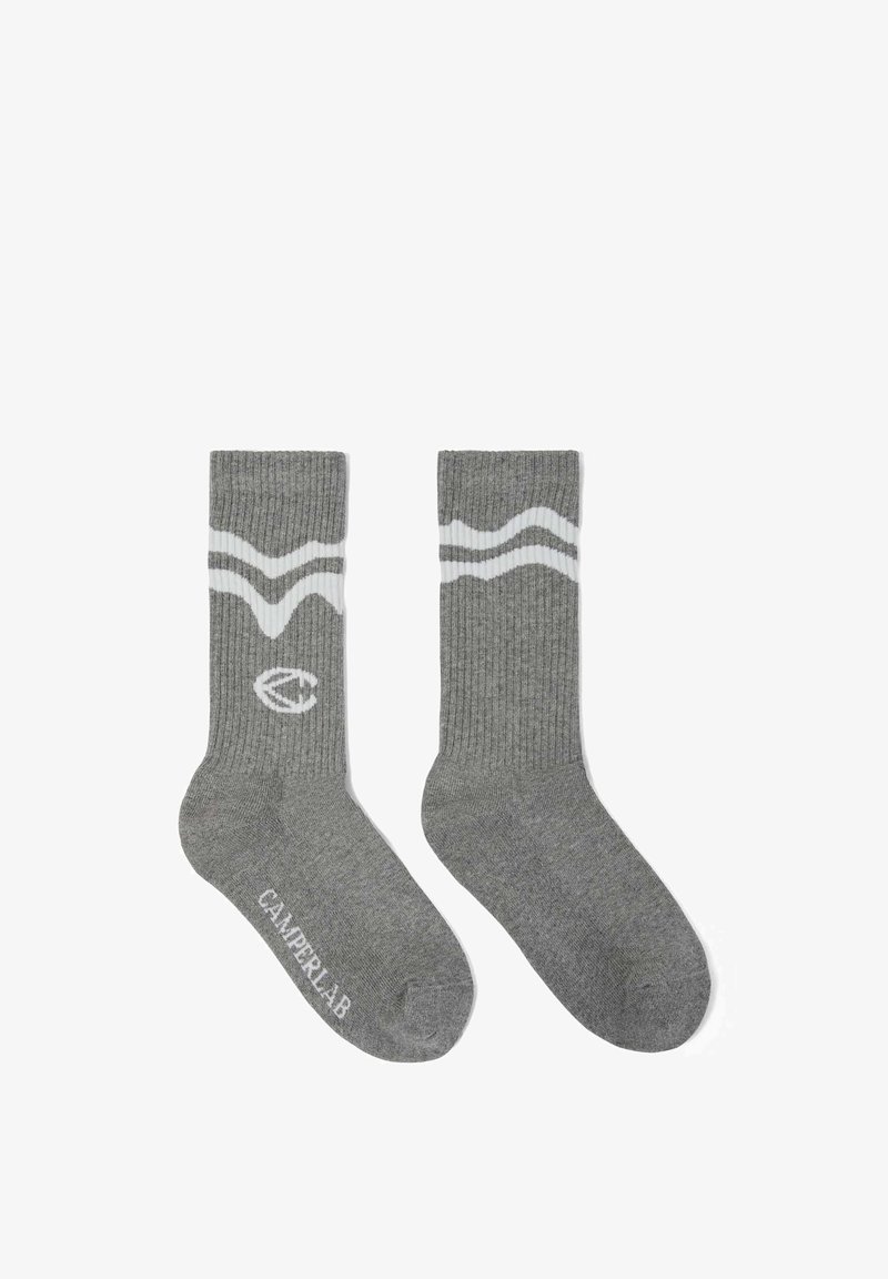 Paire de chaussettes grises côtelées montant jusqu'à la cheville, avec des rayures blanches ondulées près du haut et le texte "CAMPERLAB" sur un pied.