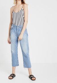 Top senza maniche a righe in bianco e nero, jeans larghi chiari con vestibilità cropped e sandali neri con dettagli in fibbia argentata.