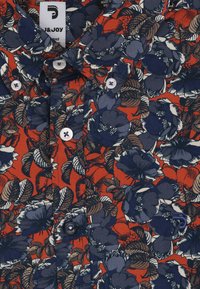 Rode bloesemshirt met blauwe en witte bloemen, met een knoopsluiting en een gestructureerde stof. De knopen zijn lichtblauw met een subtiele glans.