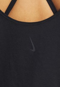 Haut de sport noir côtelé avec un décolleté arrondi et de fines bretelles. Présente un logo Nike noir discret sur le devant.
