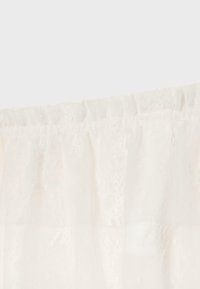 Panneau de rideau en dentelle blanche avec des motifs floraux subtils et un bord supérieur froncé pour suspendre à une tringle.