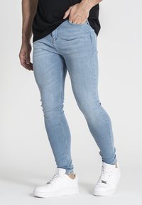 Jeans ajustados de color azul claro hechos de denim, con un diseño de cinco bolsillos y una textura suave, combinados con zapatillas blancas.