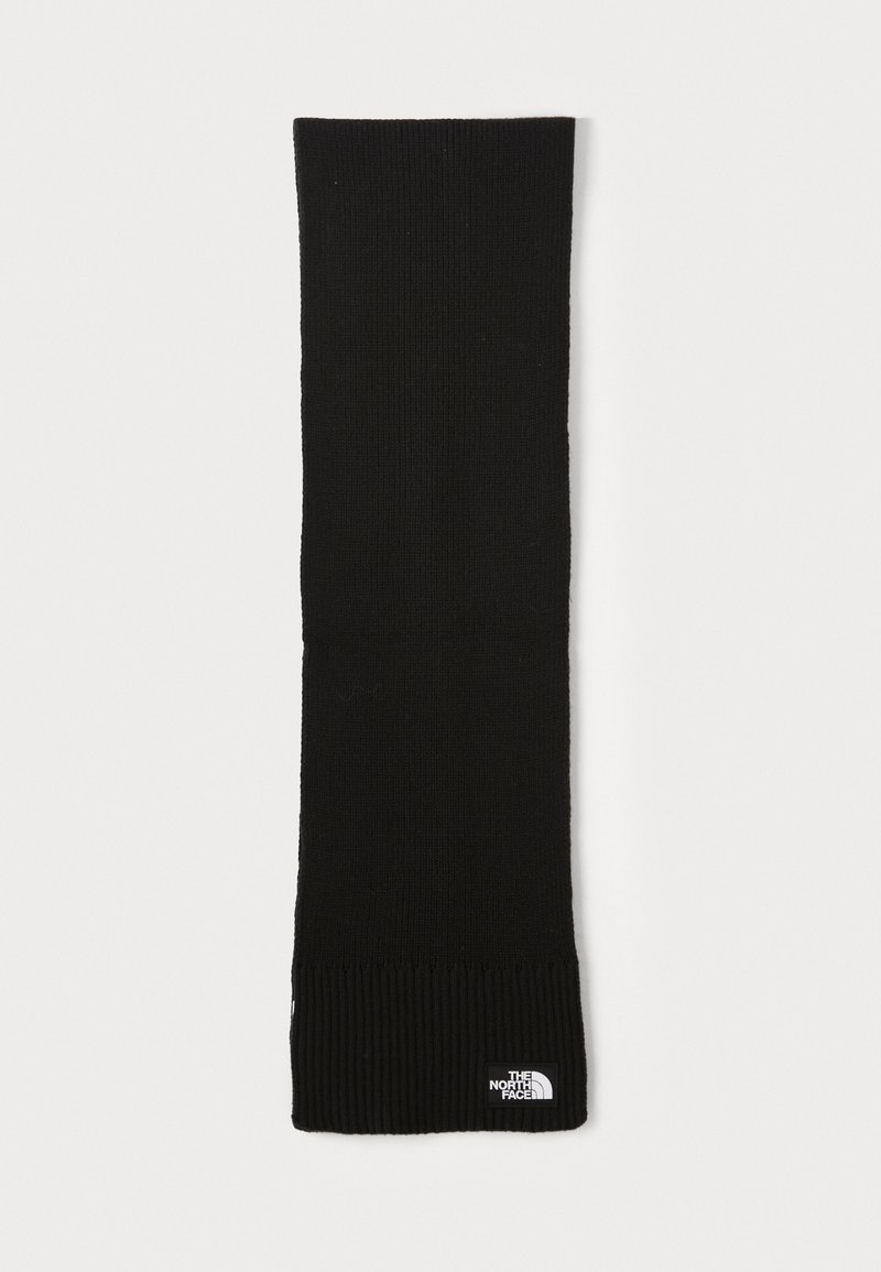 Écharpe en tricot noire avec une texture ribbed aux extrémités. Présente une petite étiquette de logo blanche. Forme longue et rectangulaire pour un port polyvalent.