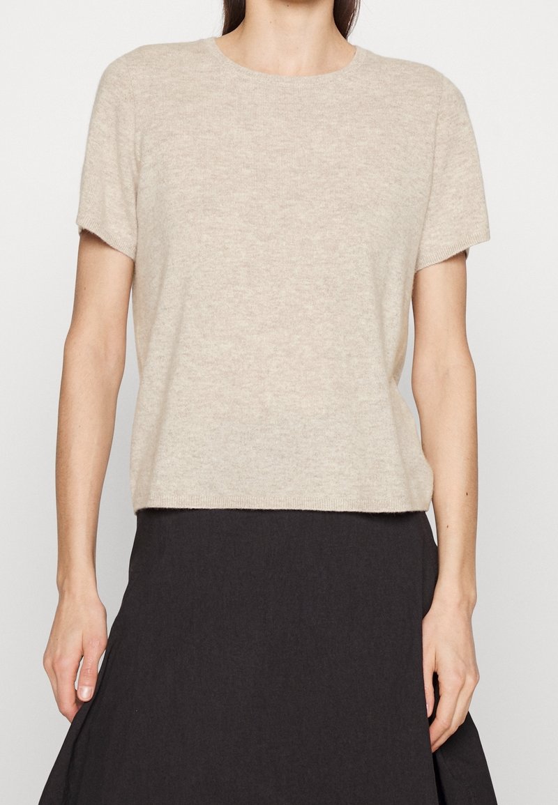 Beige kortærmet sweater lavet af blødt strikstof, med rund halsudskæring og afslappet pasform, parret med et mørkt nederdel.