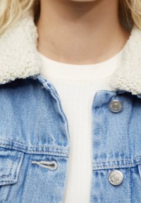 Veste en denim avec une finition bleu clair, dotée d'un col en fausse peau de mouton de couleur crème douce et de boutons en métal argenté.