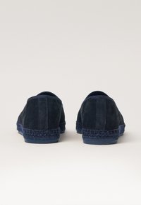 Navy blue suede shoes with a braided jute sole and rounded edges. The rear view highlights the soft texture and minimalist design.