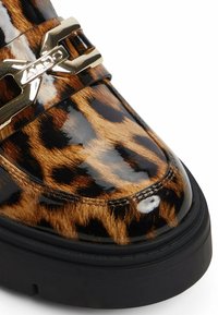 Mocassin avec un dessus en imprimé léopard brillant, semelle épaisse noire et détail en métal doré gravé "ALDO" sur la sangle.