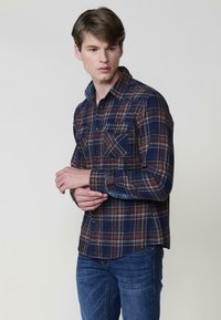 Camicia a maniche lunghe da uomo a quadri nei toni del blu, rosso e verde. Presenta due tasche sul petto, chiusura con bottoni e colletto. Tessuto in cotone, con una texture. 
