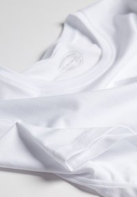 Weißes Baumwoll-T-Shirt mit Rundhalsausschnitt, das eine glatte Textur und umgeschlagene Kanten aufweist, teilweise gefaltet, um das Etikett im Inneren zu zeigen.