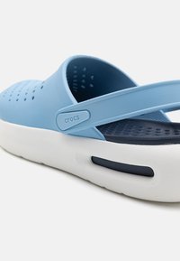 Light blue Crocs with a design featuring a wide strap, perforated upper, and a white sole with a navy accent. Textured interior for comfort.