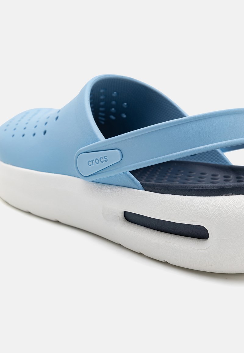 Helleblaue Crocs mit einem Design, das einen breiten Riemen, ein perforiertes Obermaterial und eine weiße Sohle mit navyblauem Akzent umfasst. Strukturiertes Innenleben für zusätzlichen Komfort.