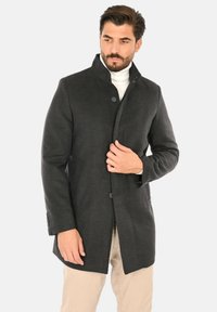 Cappotto in lana grigio scuro con collo alto, bottoni monopetto e vestibilità affusolata; presenta tasche laterali e polsini sagomati.