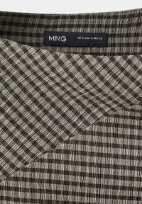 Gros plan d'un tissu texturé rayé vertical noir et gris avec une étiquette de marque MNG indiquant la taille EU S USA 4 MEX CH.