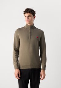 Pullover in verde oliva con mezza zip, in tessuto lavorato a maglia, con polsini e orlo a coste, caratterizzato da un piccolo logo rosso sul lato sinistro del petto.