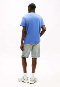 T-shirt blu a maniche corte con una finitura testurizzata, abbinato a pantaloni corti in denim chiaro. Scarpe da ginnastica bianche e verdi completano l'outfit.