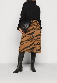Maglione nero a collo alto, gonna marrone con strisce di tigre nere, bottoni sul davanti, abbinato a stivali in pelle nera fino al ginocchio e una borsa.
