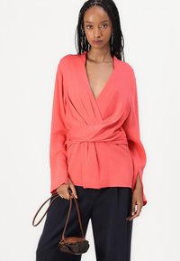 Blusa avvolgente in tessuto leggero, con scollatura a V profonda, maniche lunghe e vita legata. Abbinate a pantaloni scuri e una borsa piccola.