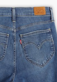 Jeans de mezclilla con un lavado azul intermedio, que cuentan con una parche de cuero, bolsillos traseros curvados y costuras en contraste. Diseño clásico de cinco bolsillos.