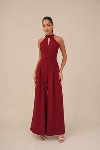 Combinaison bordeaux avec un col halter et un détail en trou de serrure, arborant des pantalons à jambes larges plissés et un corsage ajusté. Texture de tissu lisse.