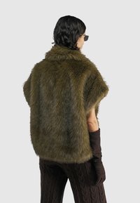 Groene nepbont gilet met een kraag en korte mouwen, gecombineerd met donkerbruine handschoenen en geblokte bruine broeken. Soepele, gestructureerde uitstraling.