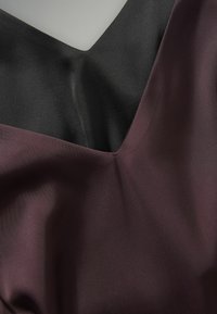 Satinové šaty s V-výstrihom, ktoré majú farebný blok v tmavobordovej a čiernej farbe. Hladká textúra, jemný lesk a elegantné splývanie.