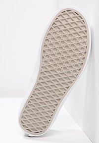 White sneaker sole with a textured, hexagonal grip pattern. The side has a smooth finish, with a slight curve at the toe.