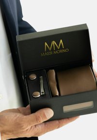 Sort boks med guld logo indeholder et brunt slips, matchende manchetknapper og en slipsenål. Har en tekstureret overflade og sikret lukning.
