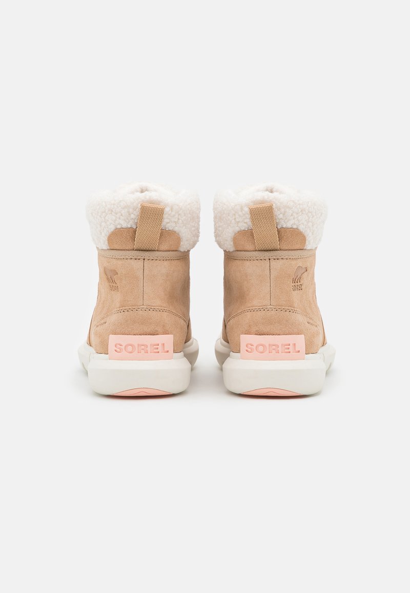 Bottes chelsea en cuir suédé beige avec un col en faux fur blanc, un logo en caoutchouc rose sur le talon et une semelle contrastante blanche et rose.