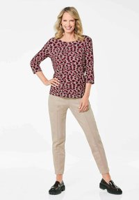 Bordeaux gemusterte Bluse mit Dreiviertelärmeln, kombiniert mit beigen Slim-Fit-Hosen und schwarzen Plateaul loafers. Glatte Textur, lässiges Design.