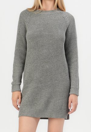 Femme portant une robe-pull en maille grise à manches longues avec des poignets et un ourlet côtelés sur un fond blanc uni.