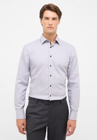 Lichtgrijs langarm shirt met een knoopsluiting kraag, voorzien van zwarte knopen en manchetten, gecombineerd met donkergrijze broek.
