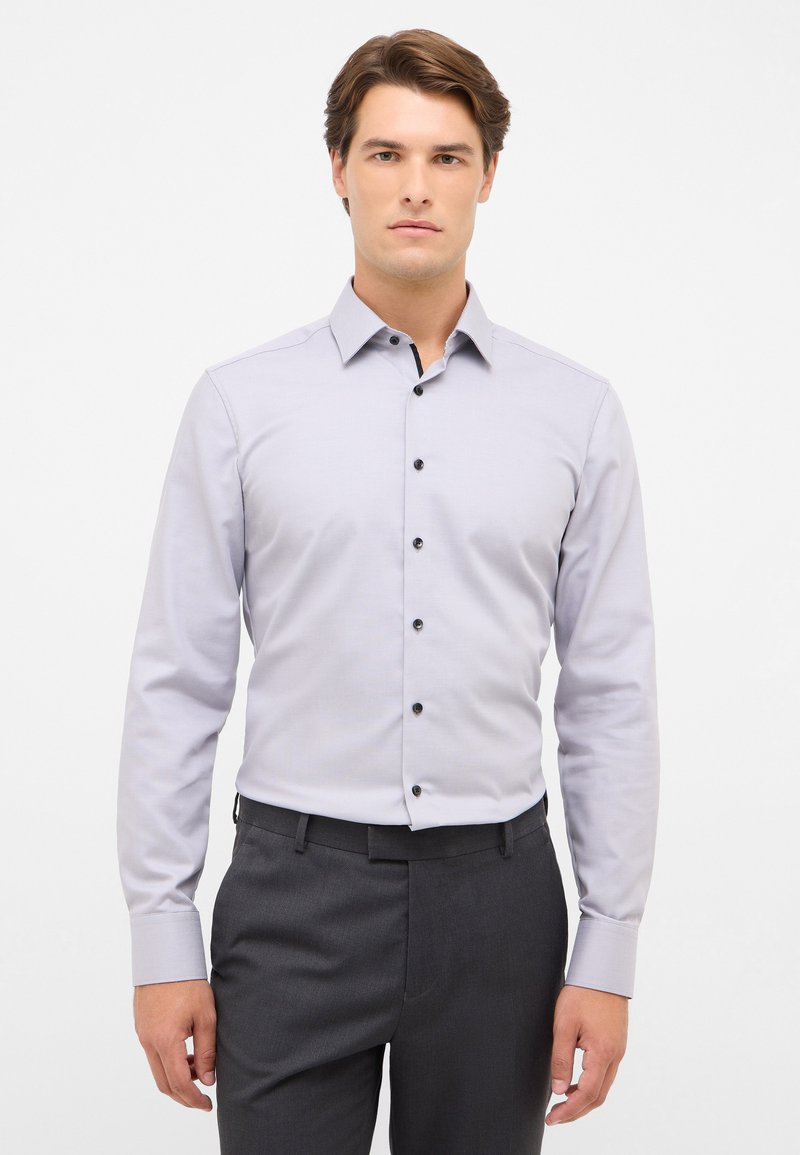 Lichtgrijs langarm shirt met een knoopsluiting kraag, voorzien van zwarte knopen en manchetten, gecombineerd met donkergrijze broek.