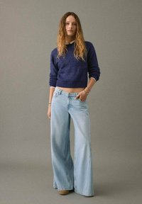 Granatowy sweter z dzianiny z okrągłym dekoltem, zestawiony z jasnoniebieskimi spodniami z wysokim stanem i szerokimi nogawkami. Spodnie mają klasyczny pięcio-kieszeniowy krój.