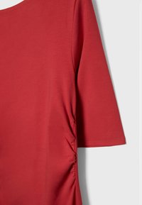 Red, short-sleeved top in a smooth, stretchy fabric. Features gathered side detail and a rounded neckline. Simple, streamlined design.