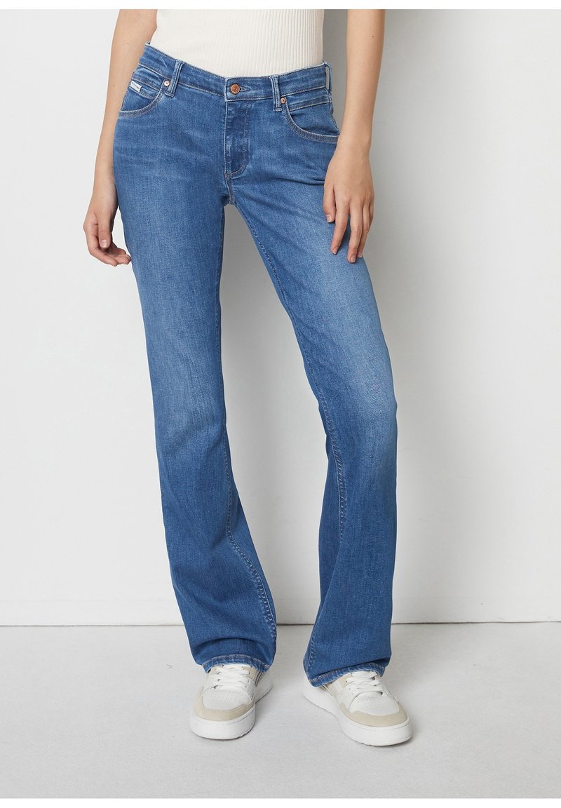 Ljusblå utsvängda jeans i denim med femficksdesign, orange sömmar och en brun metallknapp. Bärs med vita sneakers.