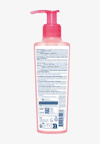 Bottiglia di plastica rosa con corpo trasparente. Etichetta con testo multilingue, ingredienti e codice QR. Tappo con pompa per erogazione.