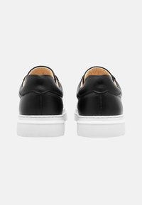 Schwarze Lederschuhe mit einer glatten Oberfläche, runder Zehenform und weißer Gummisohle. Besitzen ein dezentes, gebogenes Nahtdetail hinten.