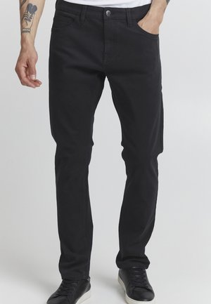 Svarta denimbyxor med smal passform, med framfickor, knappstängning och synliga sömnadsdetaljer. Kompletterade med svarta sneakers.