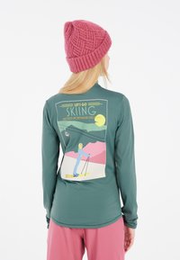 Groene longsleeve shirt met een ski-graphic op de achterkant, gecombineerd met een roze gebreide muts met structuur. Glad materiaal, relaxte pasvorm.