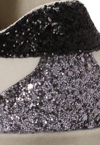 Característica del zapato: parte superior de lentejuelas negras con un detalle de lentejuelas gris texturizado. Base liza de color claro. Forma distintiva con materiales en contraste.