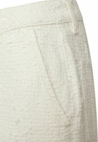 Pantaloni bianchi texturizzati con un motivo sollevato e sottile. Il tessuto appare morbido, con cuciture visibili e tasche laterali.