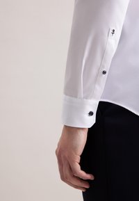 Witte langemouwen shirt met knoopmanchetten, voorzien van een kleine geborduurde bloemdetail op de manchet en een gladde textuur.