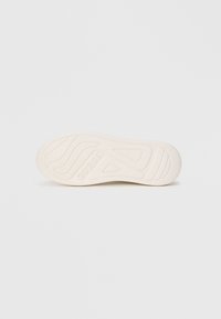 Weiße Schuhsohle mit strukturierten Mustern und dem eingeprägten Markennamen "GUESS" in der Mitte, isoliert auf einem schlichten weißen Hintergrund.