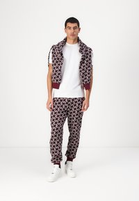 Dvoudílný outfit skládající se z vzorovaného svetrů v námořnické modré a burgundské barvě a odpovídajících tepláků, obojí vyrobené z měkké látky. Bílý tričko a tenisky.