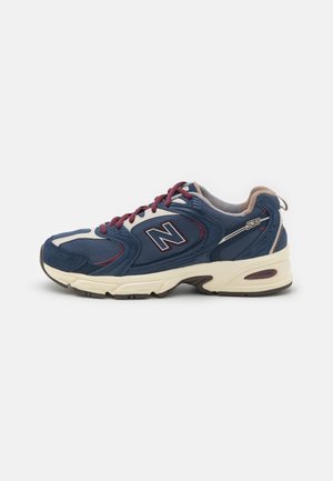 Chaussure de sport New Balance bleu et crème avec lacets et logo bordeaux, dessus en mesh et suède, semelle amortie, vue de côté.