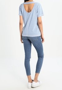 T-shirt rayé bleu et blanc avec un dos rond ouvert. Associé à un jean clair ajusté et des baskets blanches. Look simple et décontracté.