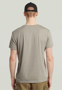 Koszulka krótki rękaw, jasnoszara, wykonana z miękkiej bawełny. Posiada okrągły dekolt i gładką fakturę. Noszona z beżowymi szortami cargo.