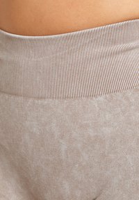 Collant da yoga beige chiaro con una ampia cintura a costine, texture liscia e una leggera variazione di colore sulla superficie del tessuto.