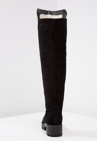 Botas de ante negras hasta la rodilla con puntera redonda, suela de goma y cuello acolchado para mayor comodidad. Textura suave con un acabado mate.