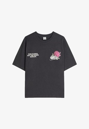Tricou negru din bumbac cu mâneci scurte. Prezintă text alb în partea stângă și o grafică florală în partea dreaptă, în nuanțe de roz și verde.